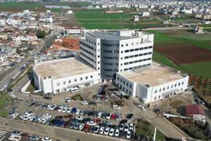 Hastane binası ve çevresindeki otopark, geniş bir alandan drone ile çekilmiş hava fotoğrafı.