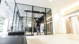 Man entering a glass-walled corporate lobby with abstract wall art and bright lighting behind it, motion blurred as he walks through the door.